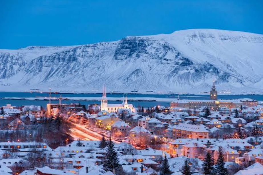 Snow-covered Reykjavik at blue hour with a white mountain ridge behind the city