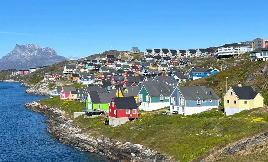 Brightly painted Nuuk houses on a green coastal slope beside an Arctic fjord
